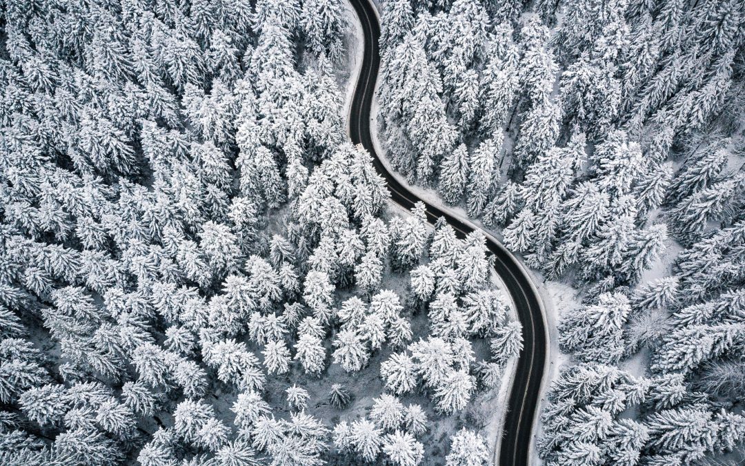 Curvy windy road in snow covered forest, top down aerial view